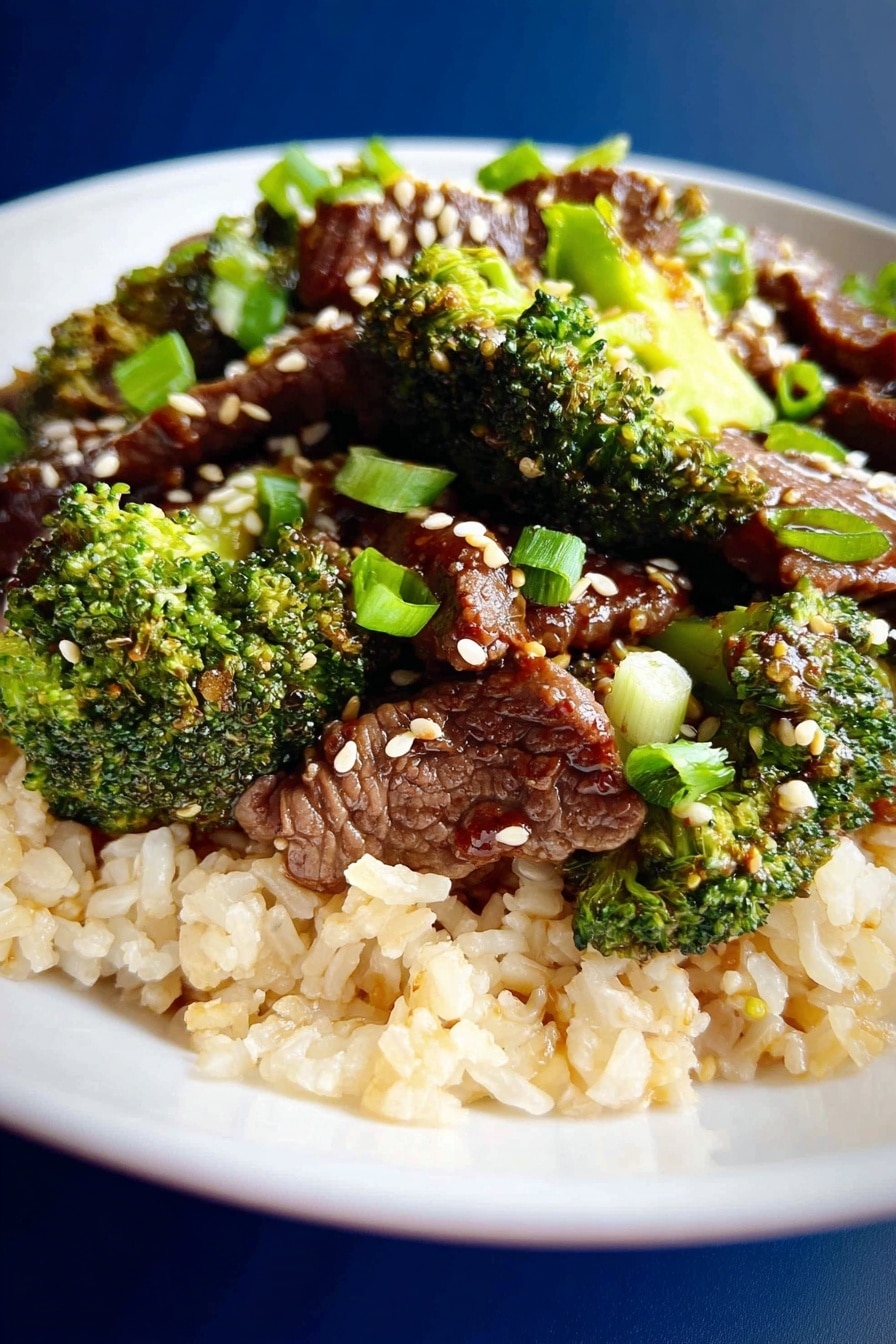 A white plate holds a bed of light brown cooked rice as the bottom layer, topped with dark brown cooked beef slices mixed with bright green broccoli florets. Scattered white sesame seeds and pale green onion slices add texture and color contrast. The background has a smooth deep blue color, and the overall look is fresh and vibrant. photo taken with an iphone --ar 2:3 --v 7 - Instant Pot Beef and Broccoli, quick beef and broccoli, easy Instant Pot dinner, healthy beef stir-fry, weeknight stir-fry recipe