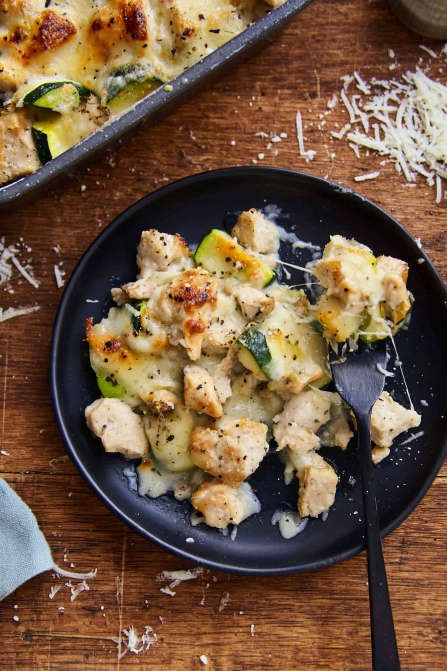 The image shows a black round plate with a serving of a baked dish made of three main visible layers. The bottom layer consists of small, uneven pieces of light beige chicken mixed with chunks of green zucchini. The middle layer is melted light golden cheese, spread unevenly, some parts browned slightly. Scattered black pepper flakes are visible on top. A black fork on the right side of the plate holds a piece of chicken and zucchini, with cheese strands stretching between the fork and plate. The plate is placed on a wooden surface with some grated white cheese scattered nearby. A covered baking dish with extra portions of the same dish is partly visible in the top left. The photo taken with an iphone --ar 2:3 --v 7 - Cheesy Chicken Zucchini Casserole, Chicken and Zucchini Bake, Easy Cheesy Chicken Dinner, Healthy Chicken Casserole, Comfort Food with Zucchini