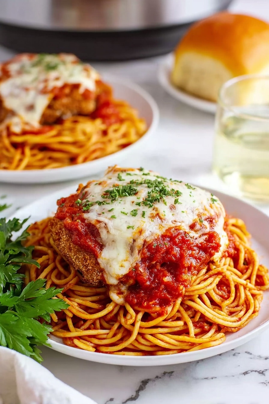 Easy Crock Pot Chicken Parmesan Recipe 8 A white plate holds a layered dish starting with a base of thin spaghetti noodles coated in bright red tomato sauce, arranged in a round nest shape. On top of the noodles lies a large breaded and fried meat cutlet covered with melted white cheese and more chunky red tomato sauce sprinkled with small green parsley bits. A sprig of fresh green parsley rests beside the plate on a white marbled surface. In the background, a second white plate holds the same dish, a glass of clear liquid, and a round golden bread roll. photo taken with an iphone --ar 2:3 --v 7 - Easy Crock Pot Chicken Parmesan, crock pot chicken parmesan, slow cooker chicken parmesan, simple chicken parmesan recipe, effortless chicken parmesan dinner