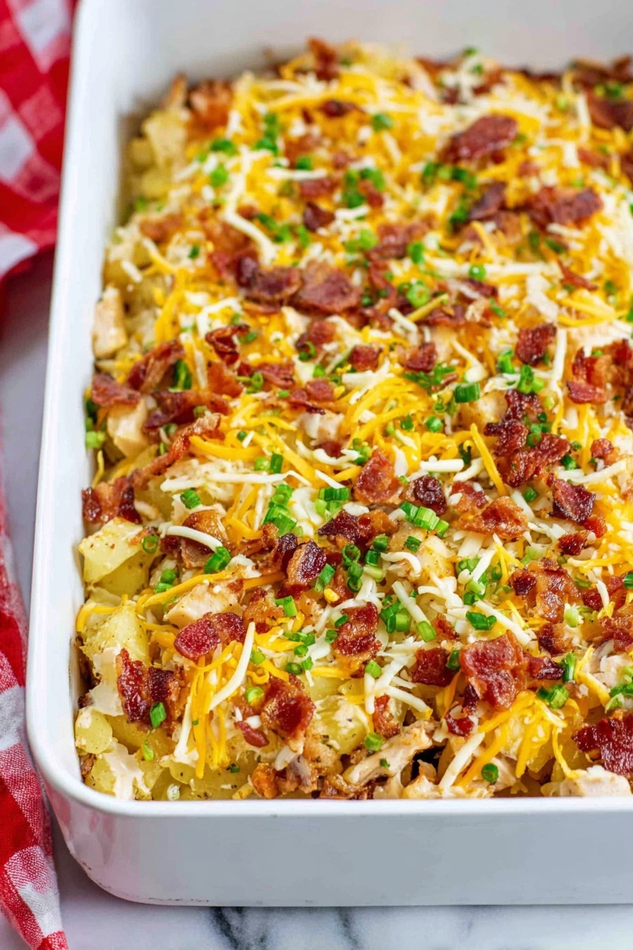 Creamy Chicken Bacon Ranch Casserole Recipe 8 A white rectangular baking dish filled with a layered casserole. The bottom layer has small golden browned potato pieces mixed with chunks of cooked chicken. On top of this, there are small pieces of cooked bacon scattered evenly. The dish is generously topped with a mix of shredded yellow and white cheeses, sprinkled with green chopped herbs. The edges of the casserole show some browning, suggesting it is baked. The white marbled surface and a red and white checkered cloth are visible in the background. Photo taken with an iphone --ar 2:3 --v 7 - Creamy Chicken Bacon Ranch Casserole, chicken bacon ranch casserole, cheesy chicken dinner, easy weeknight casseroles, comfort food recipes