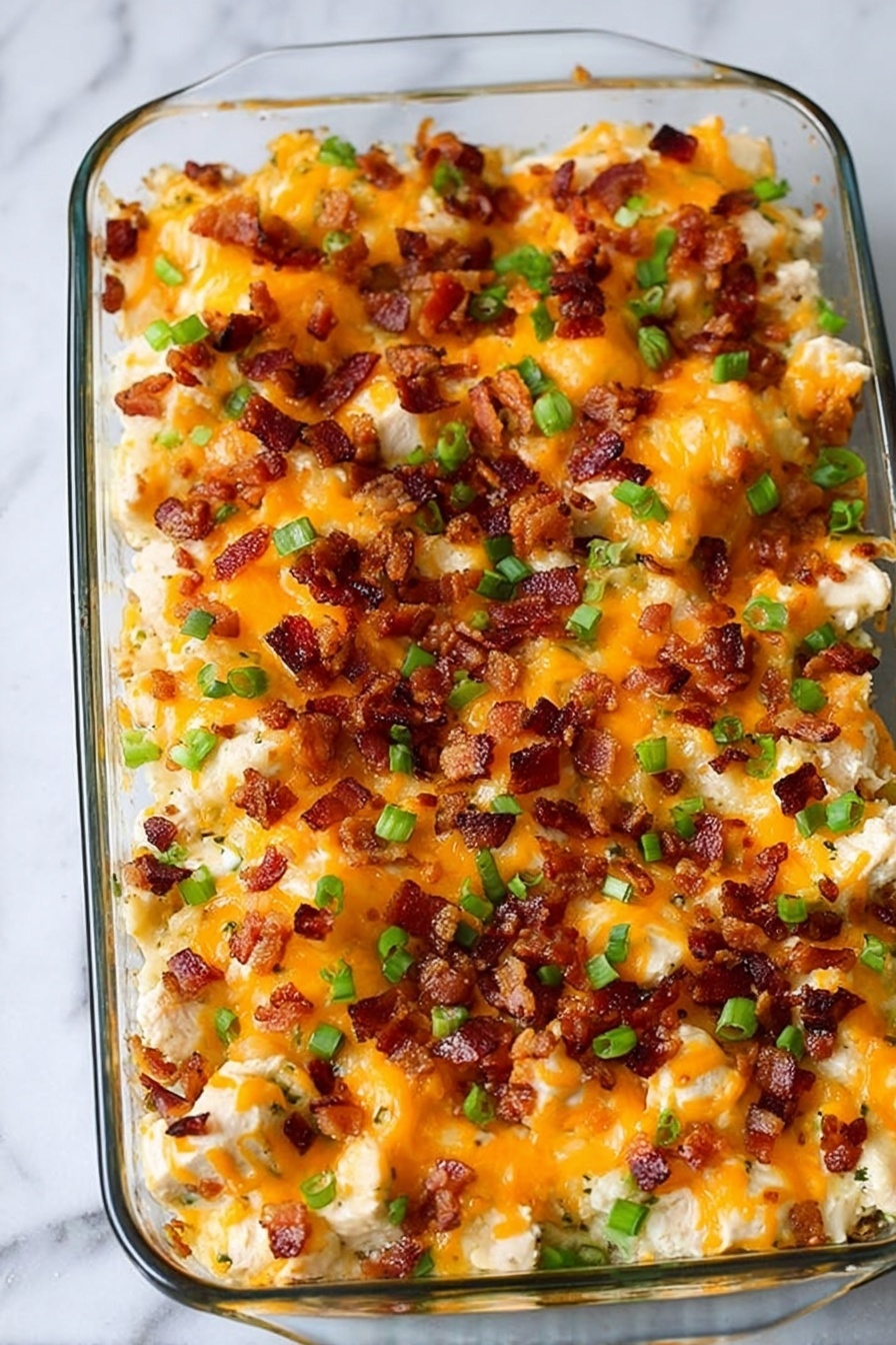 Loaded Ranch Chicken and Potato Casserole Recipe 8 A glass rectangular dish filled with a baked casserole showing three main layers: the bottom layer has small chunks of tender white chicken pieces, topped by a thick layer of melted orange cheddar cheese that covers the chicken well, and scattered on top are crisp, small dark brown bacon bits along with chopped green onions, adding bursts of green color throughout. The dish sits on a white marbled surface. Photo taken with an iphone --ar 2:3 --v 7 - Loaded Ranch Chicken and Potato Casserole, cheesy chicken and potato casserole, easy loaded baked potato casserole, ranch chicken potato bake, hearty comfort casserole