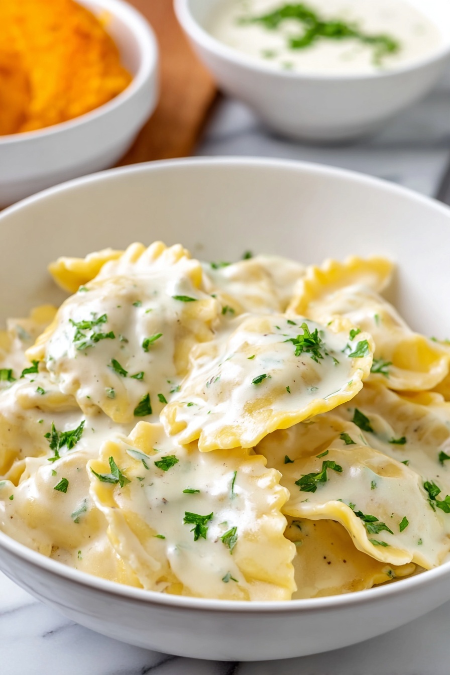Garlic Parmesan Tortellini Recipe 8 A white bowl filled with about two layers of ravioli pasta covered in a creamy white sauce with a smooth texture, sprinkled with small bright green chopped parsley leaves on top. The ravioli pieces, which are yellow with slightly wavy edges, are mostly visible under the sauce with some overlapping. In the background on a white marbled surface, there is a blurry white bowl containing a white creamy sauce and a part of an orange item. Photo taken with an iphone --ar 2:3 --v 7 - Garlic Parmesan Tortellini, easy garlic tortellini, creamy pasta recipes, quick dinner ideas, comforting pasta dish