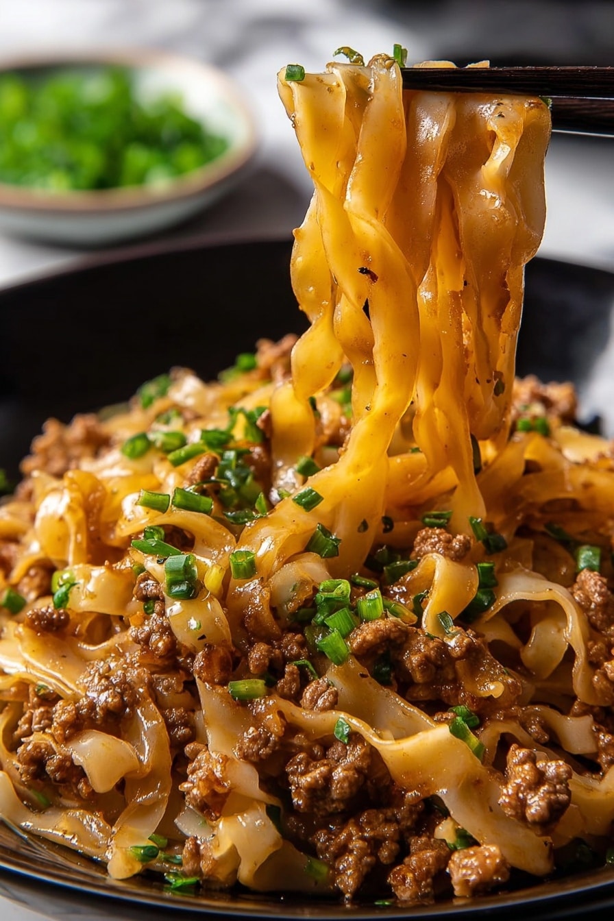 Potsticker Noodle Bowl with Pork and Green Onions Recipe 6 The image shows a close-up of a black bowl filled with thick, wide noodles mixed with small pieces of cooked ground meat, all coated in a shiny brown sauce. Small bright green chopped chives are sprinkled evenly throughout the noodles, adding color contrast. A pair of black chopsticks lifts a bunch of the noodles from the bowl, showing their soft, smooth texture and the meat clinging to them. In the blurred background, there is a small white bowl with more green chives. The surface below is a white marbled texture. photo taken with an iphone --ar 2:3 --v 7 - Potsticker Noodle Bowl with Pork and Green Onions, Asian noodle bowl with pork and green onions, quick potsticker noodle dinner, savory pork noodle bowl, easy Asian-inspired recipes