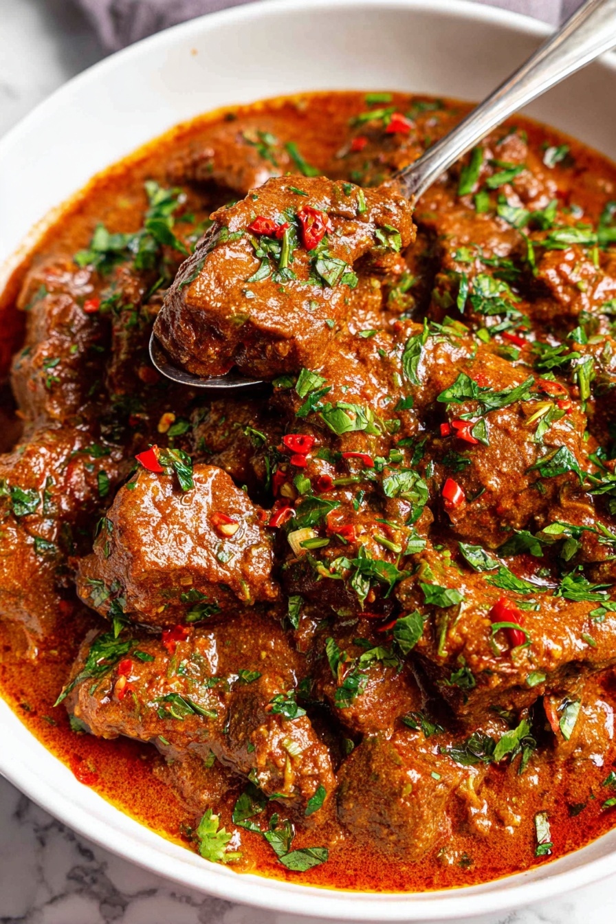 Easy Carne Guisada Recipe 6 A close-up view of a white bowl filled with a thick stew made of brown meat chunks covered in a rich, smooth reddish-brown sauce. The dish is sprinkled generously with bright green chopped herbs and small red chili flakes, adding texture and color contrast on top. A silver spoon holds a few pieces of the meat and sauce above the stew, showing the creamy consistency and tender texture of the meat. The background is a white marbled surface. photo taken with an iphone --ar 2:3 --v 7 - Carne Guisada, easy carne guisada, Tex-Mex beef stew, hearty beef stew, simple carne guisada recipe