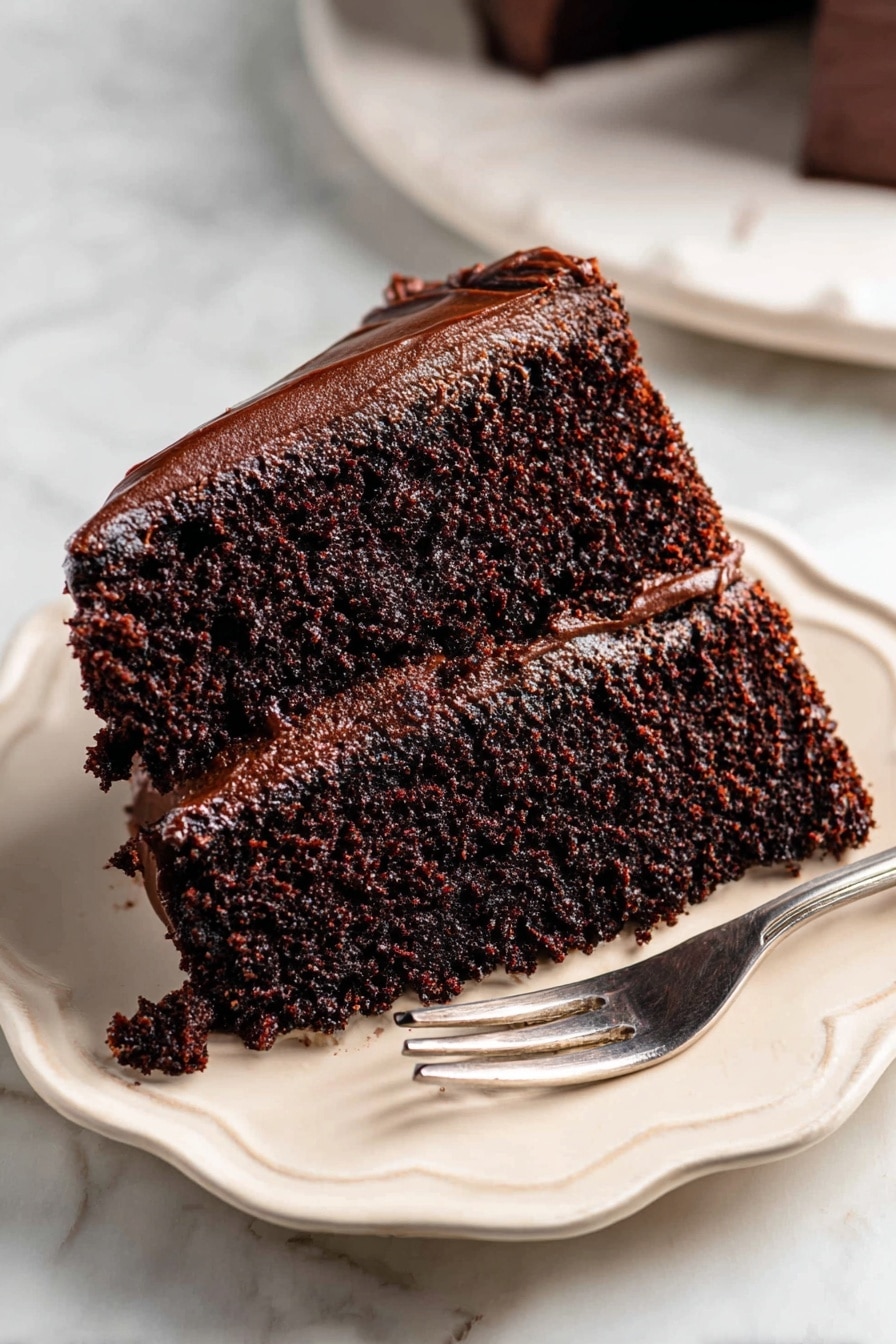 Decadent Chocolate Cake with Fudge Frosting Recipe 6 A rich chocolate cake with two thick layers covered fully in dark, shiny chocolate frosting that has large, smooth swirls and peaks all over the top and sides. A single slice is slightly pulled out from the cake, revealing the moist, dense texture inside that contrasts with the creamy, glossy frosting. The cake sits on a round white marble board on a white marbled background. Photo taken with an iphone --ar 2:3 --v 7 - Decadent Chocolate Cake with Fudge Frosting, rich chocolate cake recipe, moist chocolate cake with fudge frosting, easy chocolate cake dessert, chocolate cake with luscious frosting
