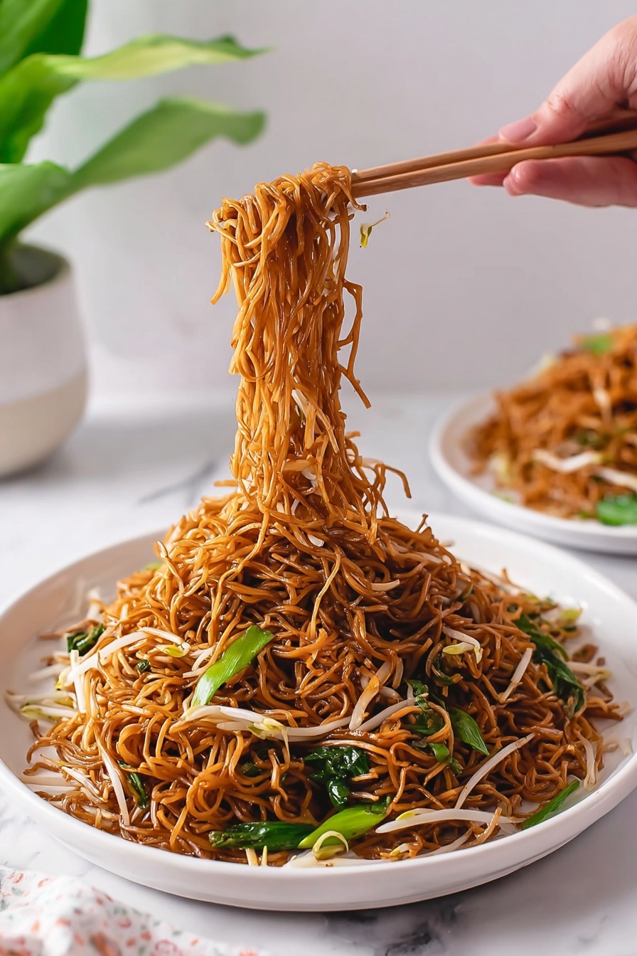 Quick Cantonese Chicken Chow Mein Recipe 8 The image shows a white deep plate filled with a large serving of brown stir-fried noodles mixed with white bean sprouts and green leafy vegetables. The noodles are thin and shiny, cooked evenly with a slight oily texture. A woman's hand is using chopsticks to lift a tangled bundle of the noodles from the center, showing the pile of noodles below still resting on the plate. In the background, there is another white plate with more noodles, and a green plant sits next to it, all placed on a white marbled surface. The scene is bright and clean with soft natural light. photo taken with an iphone --ar 2:3 --v 7 - Quick Cantonese Chicken Chow Mein, Easy Asian Chicken Noodle Stir-Fry, 15-Minute Chicken Chow Mein, Restaurant-Quality Chicken Chow Mein, Quick Weeknight Dinner Recipes