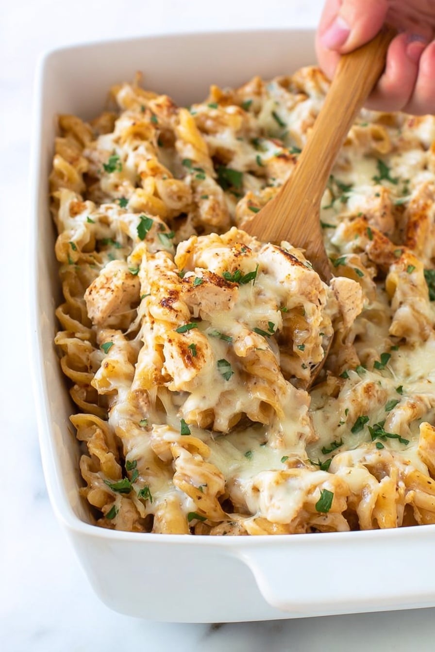 Cajun Chicken Pasta Bake Recipe 6 A white rectangular dish filled with a creamy baked pasta dish. The pasta is a mix of short, curly pieces coated in a light brown sauce with melted white cheese spread unevenly on top. Small pieces of cooked chicken are mixed in with the pasta, and a few green herbs are sprinkled across for garnish. A wooden spoon is scooping some of the pasta from the dish, held by a woman's hand. The background is a white marbled surface. photo taken with an iphone --ar 2:3 --v 7 - Cajun Chicken Pasta Bake, Cajun Chicken Pasta, Creamy Cajun Pasta Recipe, Baked Cajun Chicken Pasta, Easy Cajun Pasta Dish