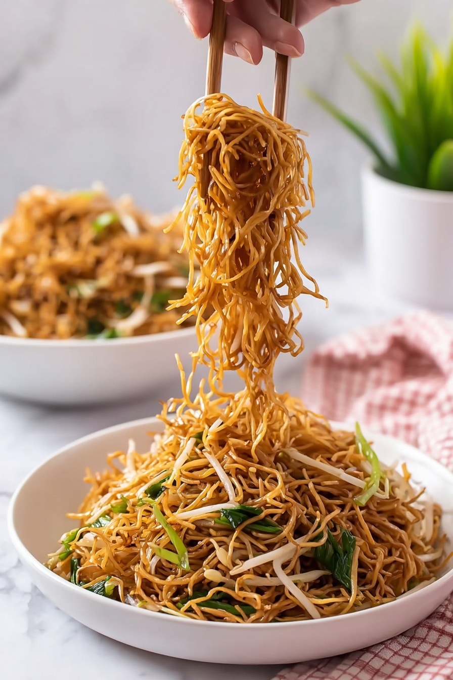 Cantonese Chow Mein Recipe 8 A white bowl filled with thin fried noodles that are golden-brown in color. Mixed within the noodles are light-colored bean sprouts and green leafy vegetables adding texture and color contrast. A woman's hand uses wooden chopsticks to lift a tangled portion of noodles above the bowl, showing the strands hanging freely. In the blurred background, there is another white bowl filled with more noodles and a green plant in a white pot. The scene is set on a white marbled surface with a soft pink and white checkered cloth at the bottom corner. Photo taken with an iphone --ar 2:3 --v 7 - Cantonese Chow Mein, Chow Mein recipe, crispy Chinese noodles, stir-fried vegetable noodles, homemade Cantonese noodle dish
