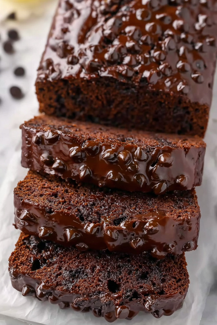 Healthy Chocolate Banana Bread Recipe 6 This image shows a loaf of chocolate bread with five thick slices stacked slightly on top of each other on white parchment. The bread is dark brown with a moist texture and embedded chocolate chips. The top of each slice is covered with a glossy layer of melted chocolate and sprinkled with more chocolate chips, giving a rich and shiny look. The background is a white marbled surface. photo taken with an iphone --ar 2:3 --v 7 - Healthy Chocolate Banana Bread, healthy banana bread, chocolate banana bread, nutritious banana cake, low-sugar chocolate bread