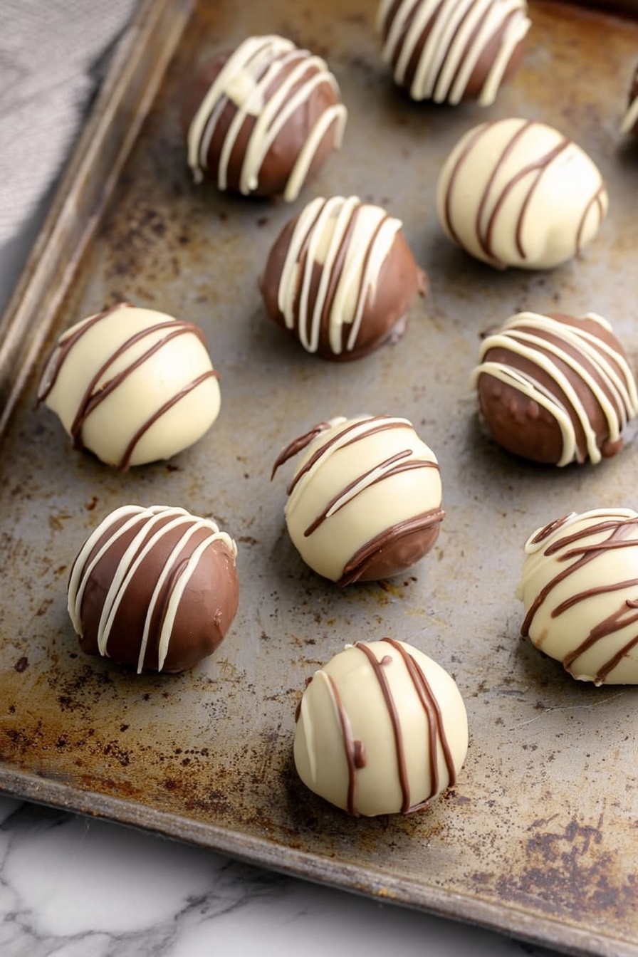 Bailey’s Irish Cream Truffles Recipe 8 Round chocolate balls are placed on a worn metal baking tray with a rustic look, sitting on a white marbled surface. Each ball has two visible layers: a smooth outer chocolate coating in either creamy white or milk chocolate brown, with neat contrasting drizzle lines on top. The white-coated balls have thin brown lines, and the brown-coated balls have white lines. The balls have a shiny, smooth texture, evenly spaced on the tray. photo taken with an iphone --ar 2:3 --v 7 - Bailey’s Irish Cream Truffles, Irish cream truffles, boozy chocolate truffles, easy Bailey’s truffles, homemade Irish cream treats