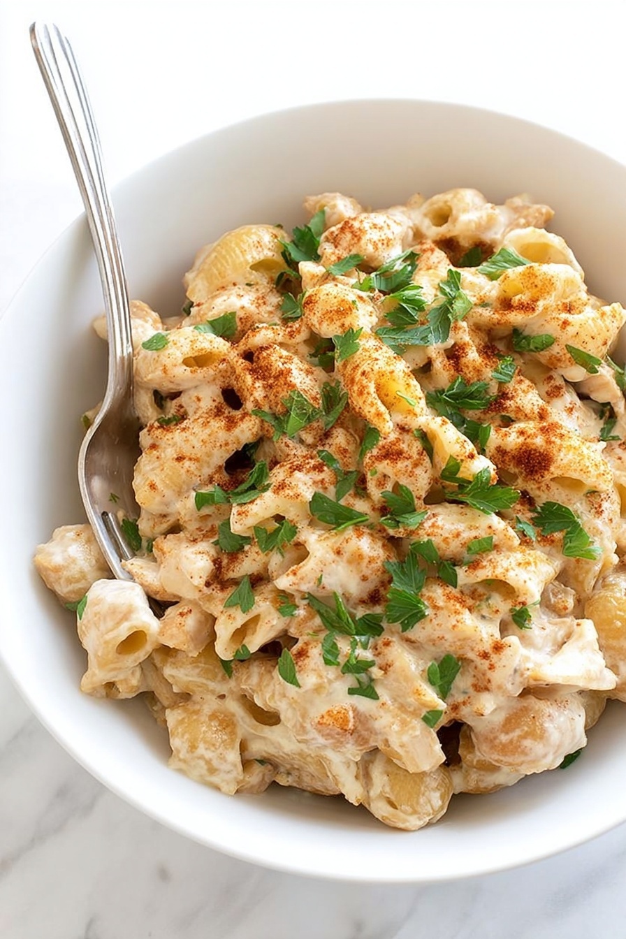 Cajun Chicken Pasta Bake Recipe 8 A white bowl filled with three layers of food, starting with a bottom layer of creamy beige pasta shells mixed with small pieces of light brown chicken. The next layer shows the pasta and chicken coated with a thick creamy sauce that has a light off-white color. The top layer is sprinkled with fresh green parsley leaves and a dusting of reddish-brown spices. A silver fork rests on the left side of the bowl. The background is a white marbled texture. photo taken with an iphone --ar 2:3 --v 7 - Cajun Chicken Pasta Bake, Cajun Chicken Pasta, Creamy Cajun Pasta Recipe, Baked Cajun Chicken Pasta, Easy Cajun Pasta Dish