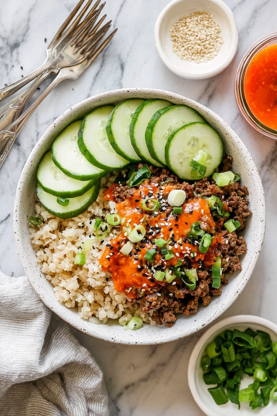 Korean Beef Bowls with Gochujang Recipe 6 A white speckled bowl contains three main layers arranged side by side: on the left, a bed of light brown rice with a soft, grainy texture; in the middle, a layer of cooked ground meat mixed with small pieces of translucent cooked onion, all topped with a drizzle of bright orange-red sauce, sprinkled with black and white sesame seeds, and garnished with small slices of fresh green scallions; on the right, five overlapping slices of fresh cucumber with pale green flesh and dark green skin. The bowl sits on a white marbled surface with a light grey cloth napkin and two silver forks beside it. Around the bowl are small white dishes, one with light sesame seeds and another with chopped green scallions, and a small glass container with orange-red sauce. photo taken with an iphone --ar 2:3 --v 7 - Korean Beef Bowls with Gochujang, Korean beef bowl recipe, spicy beef bowls, easy Korean dinner, flavorful Korean bowls