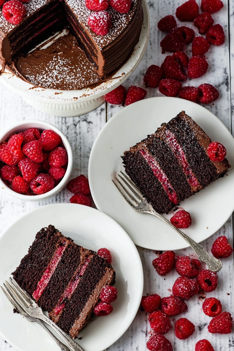 Decadent Chocolate Raspberry Layer Cake Recipe 6 A rich chocolate cake with three layers, each dark brown and moist, separated by thin layers of bright red raspberry filling; the cake is fully covered in smooth chocolate frosting and topped with fresh raspberries and a light dusting of powdered sugar. Two slices of the cake lie on white plates, each slice showing the clear layers and some raspberry pieces on the side, with silver forks resting beside them. Nearby, a white bowl is filled with fresh red raspberries scattered on a white marbled surface that the plates and cake are set on. photo taken with an iphone --ar 2:3 --v 7 - Decadent Chocolate Raspberry Layer Cake, chocolate raspberry cake, layered berry chocolate cake, easy chocolate raspberry dessert, indulgent berry chocolate cake