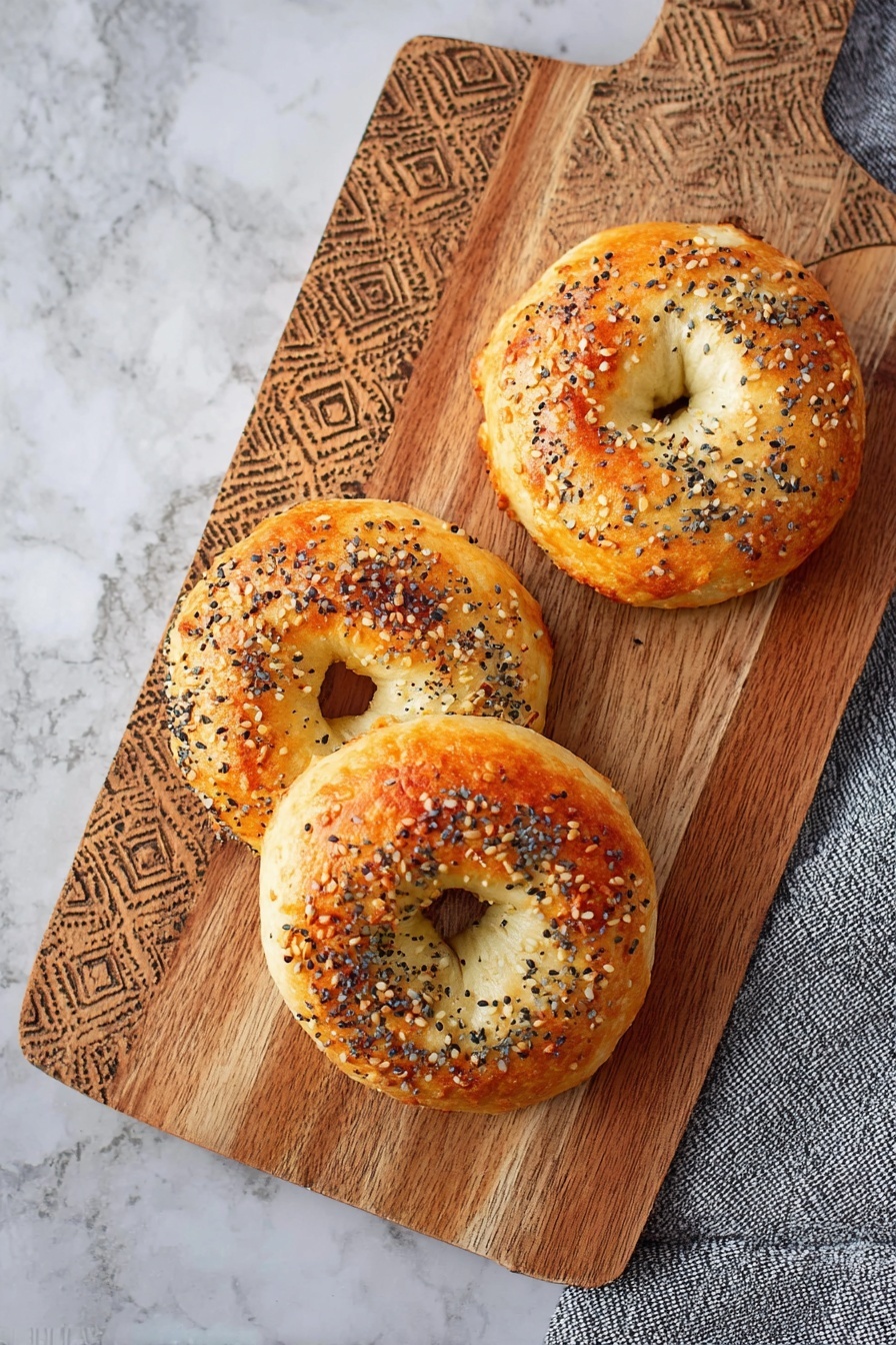 The image shows three round bagels with a golden brown top crust and a soft light beige inside, sprinkled with white sesame seeds and small black poppy seeds on top. Each bagel has a slightly shiny and textured crust with some uneven golden spots and a soft, fluffy, and slightly torn look around the edges and the hole in the middle. The bagels are placed directly on a wooden surface with a carved geometric pattern and some scattered seeds around them. The overall color is warm with natural light highlighting the texture of the bread. photo taken with an iphone --ar 2:3 --v 7 - Protein Bagel, Protein Bagel Rezept, gesunder Frühstücksbagel, proteinreiches Frühstück, einfache Bagel Rezepte