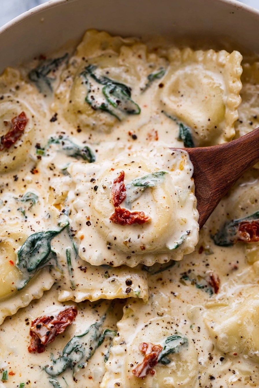 A close-up of ravioli pasta in a creamy white sauce with visible specks of black pepper and herbs. The ravioli are square with ruffled edges, covered in a thick, smooth, off-white sauce that has a rich texture. Scattered throughout the sauce are dark green wilted spinach leaves and small pieces of red sun-dried tomatoes, adding color contrast. A wooden spoon is lifting one ravioli with the creamy sauce dripping slightly, showing the pasta's soft texture. The dish sits on a white marbled surface. Photo taken with an iphone --ar 2:3 --v 7 - Creamy Tuscan Garlic Ravioli, easy Tuscan pasta recipe, quick creamy ravioli dinner, Italian-inspired Ravioli dish, flavorful garlic sauce pasta