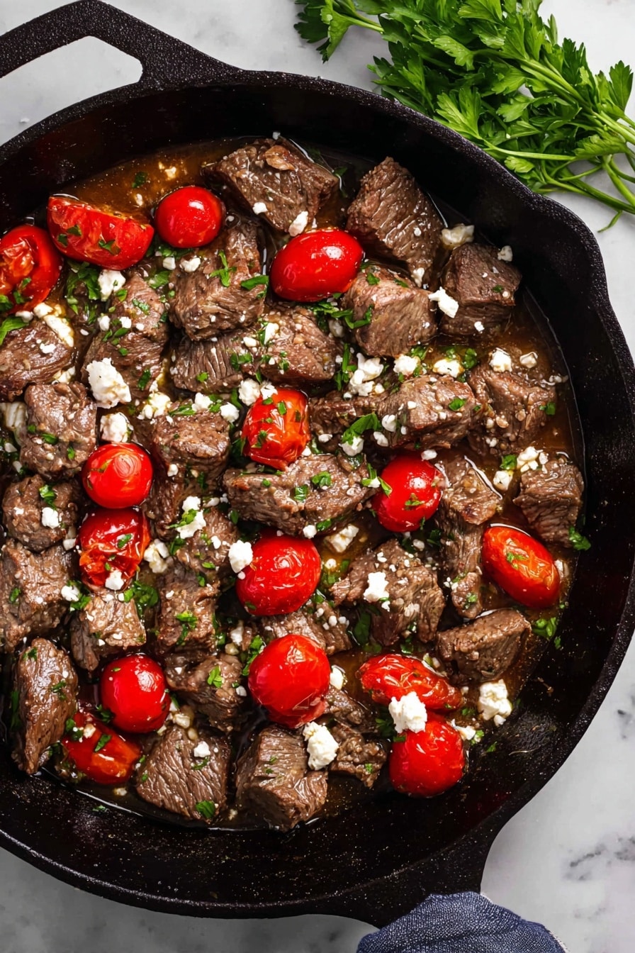 Mediterranean Steak Bites with Yogurt Sauce Recipe 6 The image shows a cast iron pan filled with medium brown cooked meat chunks scattered evenly across the pan. Among the meat chunks, several bright red cherry tomatoes, some whole and some sliced in half, add vibrant color. Small green parsley leaves are sprinkled throughout, alongside crumbled white cheese dots that create contrast against the meat. The pan sits on a white marbled surface with a small green parsley sprig placed nearby. The overall texture looks juicy with a bit of sauce pooling at the bottom. Photo taken with an iphone --ar 2:3 --v 7 - Mediterranean Steak Bites, Mediterranean Steak Bites with Yogurt Sauce, quick steak recipes, easy Mediterranean dinner, flavorful steak bites