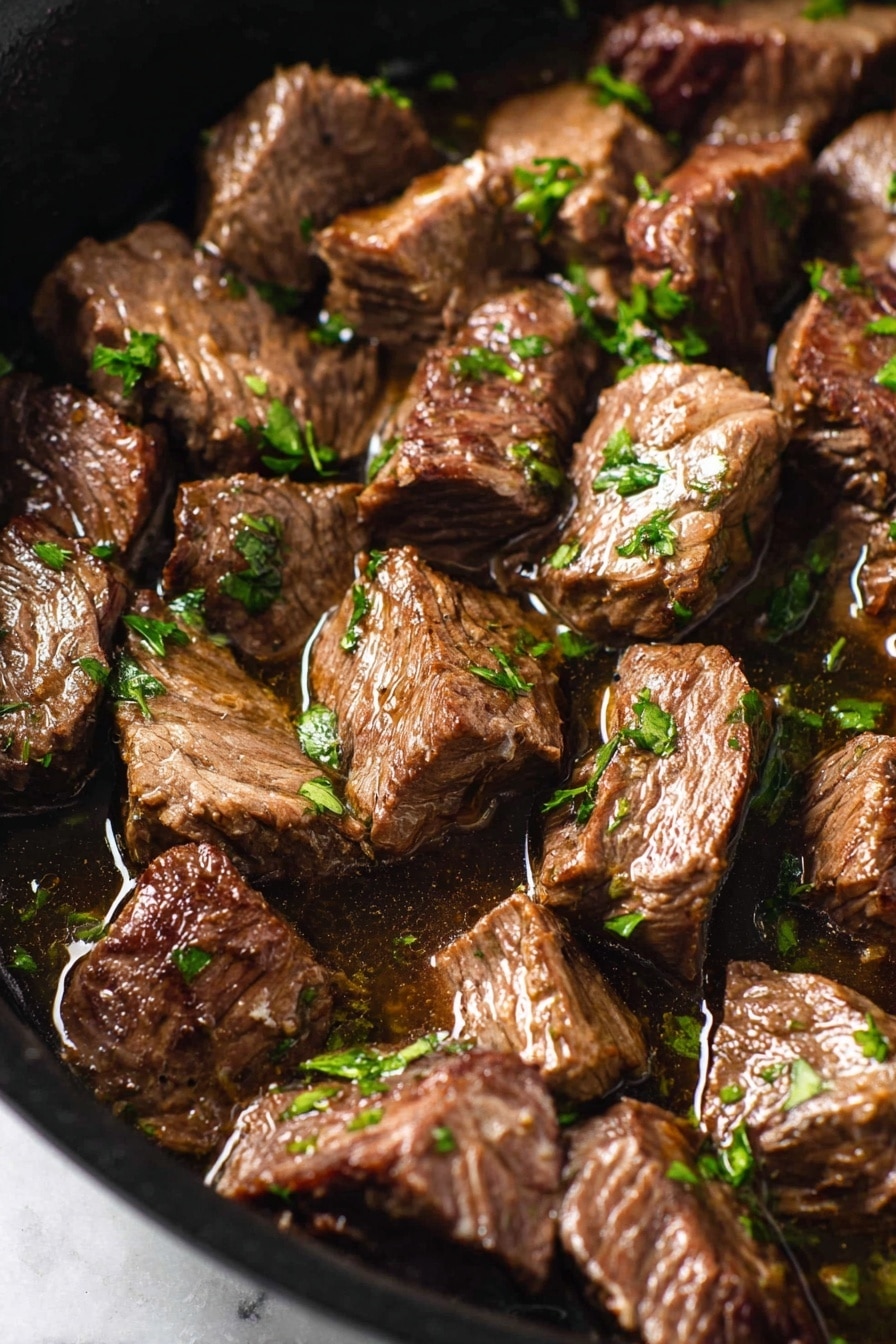 Mediterranean Steak Bites with Yogurt Sauce Recipe 8 This image shows a close-up of many pieces of cooked beef stew in a pan. Each beef piece is brown with slight darker grill marks and looks soft and juicy, sitting in a shiny broth. Small bits of bright green parsley are scattered evenly over the beef, adding a fresh touch. The pan is black and visible only around the edges, with the image set on a white marbled surface. The lighting makes the beef shine a little, showing its tender texture. photo taken with an iphone --ar 2:3 --v 7 - Mediterranean Steak Bites, Mediterranean Steak Bites with Yogurt Sauce, quick steak recipes, easy Mediterranean dinner, flavorful steak bites