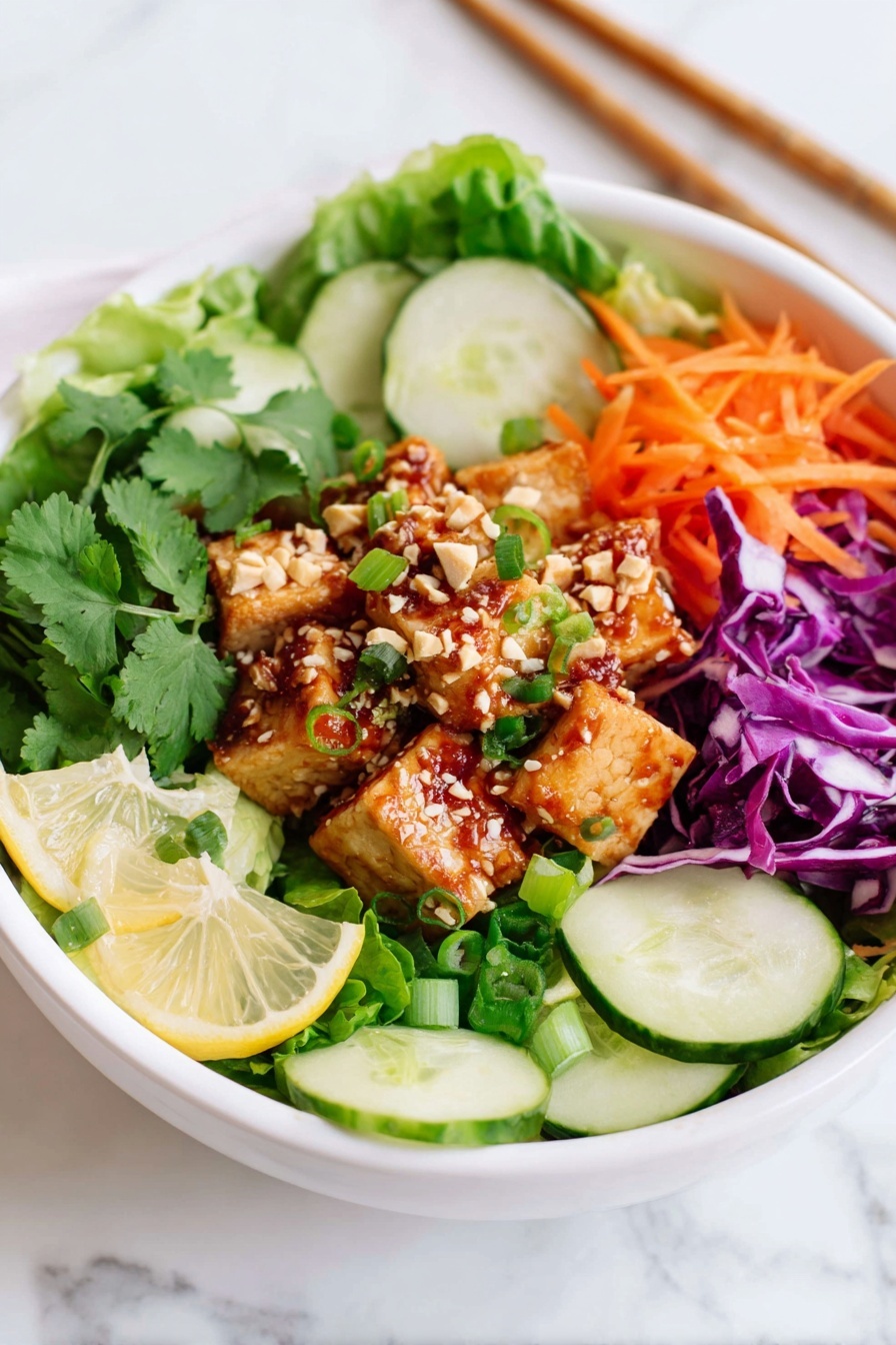 A white bowl holds a colorful salad with different layers. The bottom layer is green lettuce leaves that fill the base. Sliced cucumber rounds, bright orange carrot strips, and purple cabbage pieces sit on the edges along with green onion slices. In the center, there are small golden brown cubes of tofu dressed with a reddish sauce, topped with sesame seeds and peanuts. Fresh green cilantro sprigs decorate the top and lemon wedges are placed near the sides. The bowl rests on a white marbled surface with chopsticks visible in the back. Photo taken with an iphone --ar 2:3 --v 7 - Spicy Tofu Salad Bowls, healthy tofu salad, quick vegetarian dinner, crunchy veggie bowls, flavorful tofu recipes