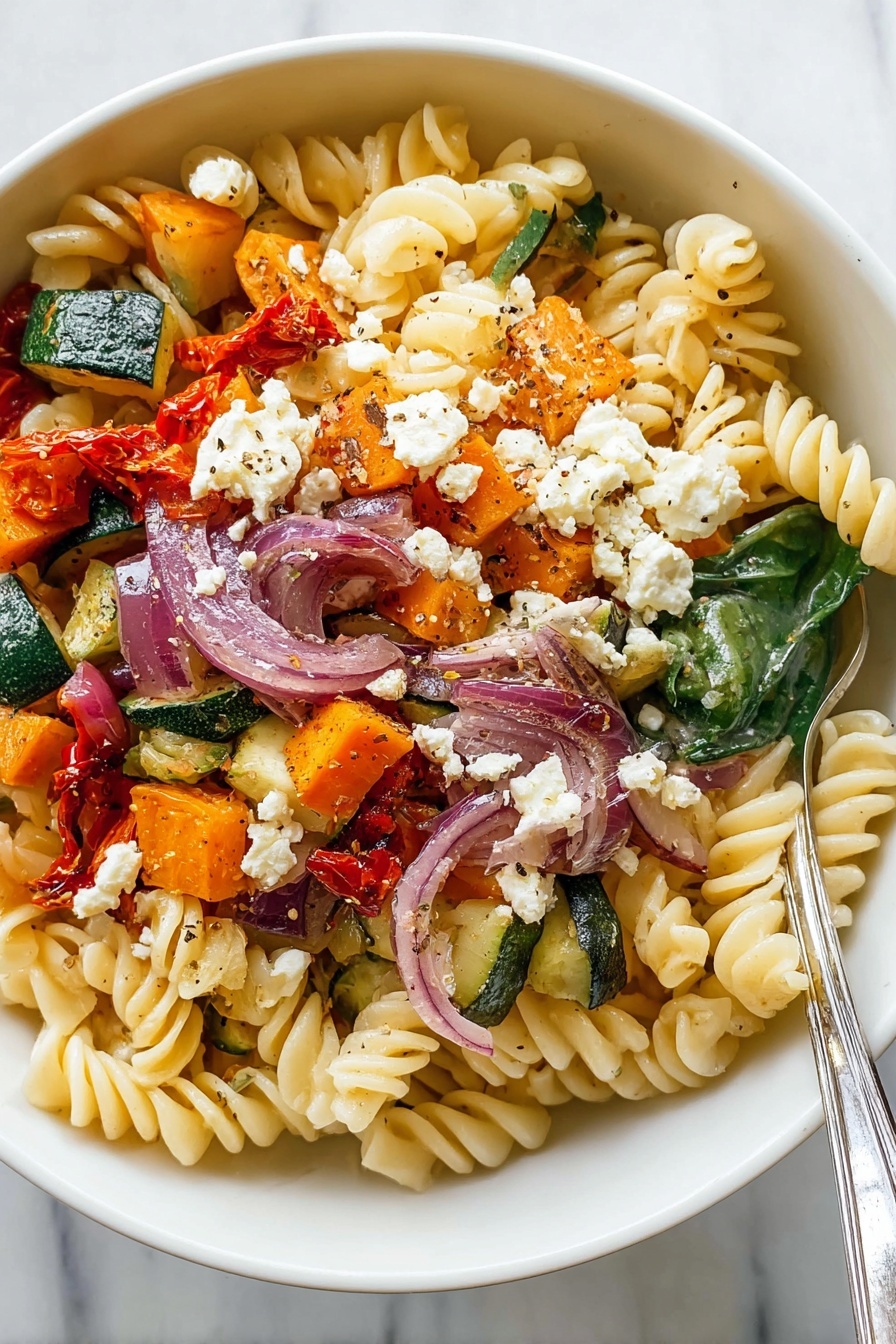 The image shows a bowl of pasta salad with three main layers. At the base, there is a layer of light yellow spiral pasta with a soft texture. On top of the pasta, there are colorful vegetables scattered: green zucchini chunks, orange sweet potato pieces, slices of red onions, and some wilted spinach leaves. The top layer has some crumbled white cheese, small roasted red pepper pieces, and a sprinkle of black pepper for seasoning. The bowl is white and the surface background has a white marbled texture. A silver fork rests inside the bowl on the right side. Photo taken with an iphone --ar 2:3 --v 7 - Roasted Veggie Pasta with Feta, roasted vegetable pasta, healthy pasta recipes, quick dinner ideas, feta pasta dishes