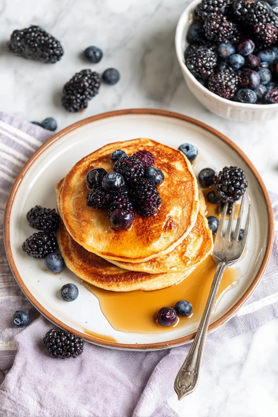 Cottage Cheese Pancakes Recipe 8 A stack of four golden brown pancakes sits in the middle of a white plate with a brown rim. The pancakes are slightly different sizes, layered unevenly, with the top pancake drenched in amber syrup that glistens under the light. Dark blackberries and plump blueberries are scattered on top of the stack and around the plate, adding deep purple and blue color. A silver fork rests on the right side of the plate, partly on a light purple and white striped cloth. In the upper right corner, a white bowl also holds a mix of blackberries and blueberries. The whole scene is set against a white marbled surface, giving a clean, bright look. photo taken with an iphone --ar 2:3 --v 7 - Cottage Cheese Pancakes, easy cottage cheese pancakes, healthy breakfast pancakes, fluffy cottage cheese pancakes, protein-packed pancake recipe