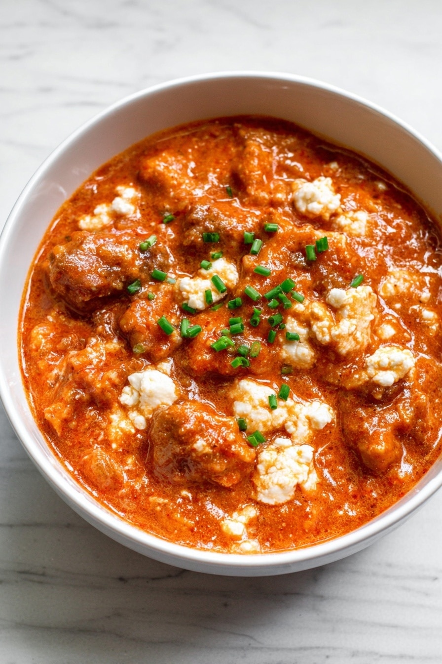 The image shows a white bowl filled with a thick mix of orange-red sauce coating small white curd-like pieces and chopped green herbs. The sauce looks creamy and slightly chunky, with the white bits spread evenly through the mixture, making it look textured and rich. A gold spoon is partially visible on the right side, partly dipped into the bowl. The bowl sits on a white marbled surface. photo taken with an iphone --ar 2:3 --v 7 - High Protein Chicken Parm Bowl, chicken parmesan bowl, healthy protein-packed dinner, quick chicken parm, nutritious Italian-inspired bowl