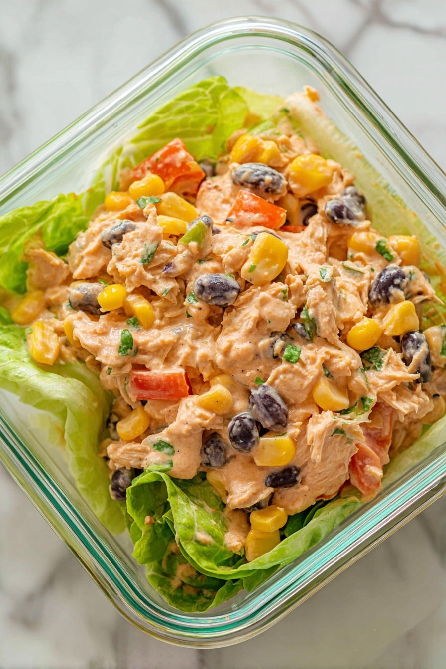Chipotle Lime Chicken Salad Recipe 8 The image shows a dish in a clear glass square container placed on a white marbled surface. The dish has three main layers: a base of light green romaine lettuce leaves, a middle layer of shredded light brown chicken mixed with chunks of bright yellow corn, diced orange bell peppers, and whole black beans, all coated with a creamy, light orange sauce that has a smooth texture. There are small green herb bits scattered throughout the mix. The whole dish looks fresh and colorful with the contrast of the sauce and vegetables against the green lettuce. Photo taken with an iphone --ar 2:3 --v 7 - Chipotle Lime Chicken Salad, healthy chicken salad recipes, smoky chicken salad, easy summer salads, flavorful chicken salad ideas